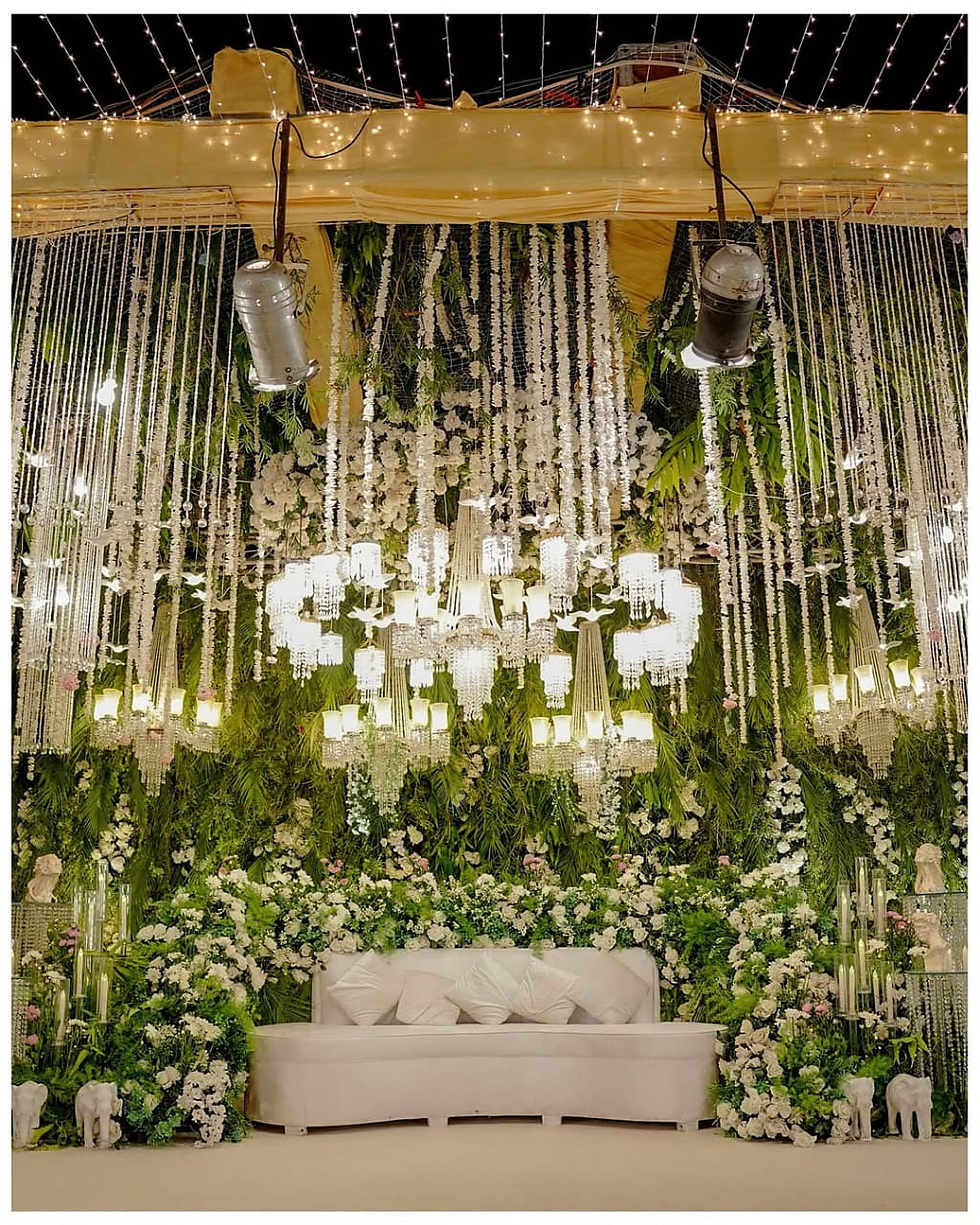 Hanging crystal columns and cascading greenery framing an ivory sofa stage