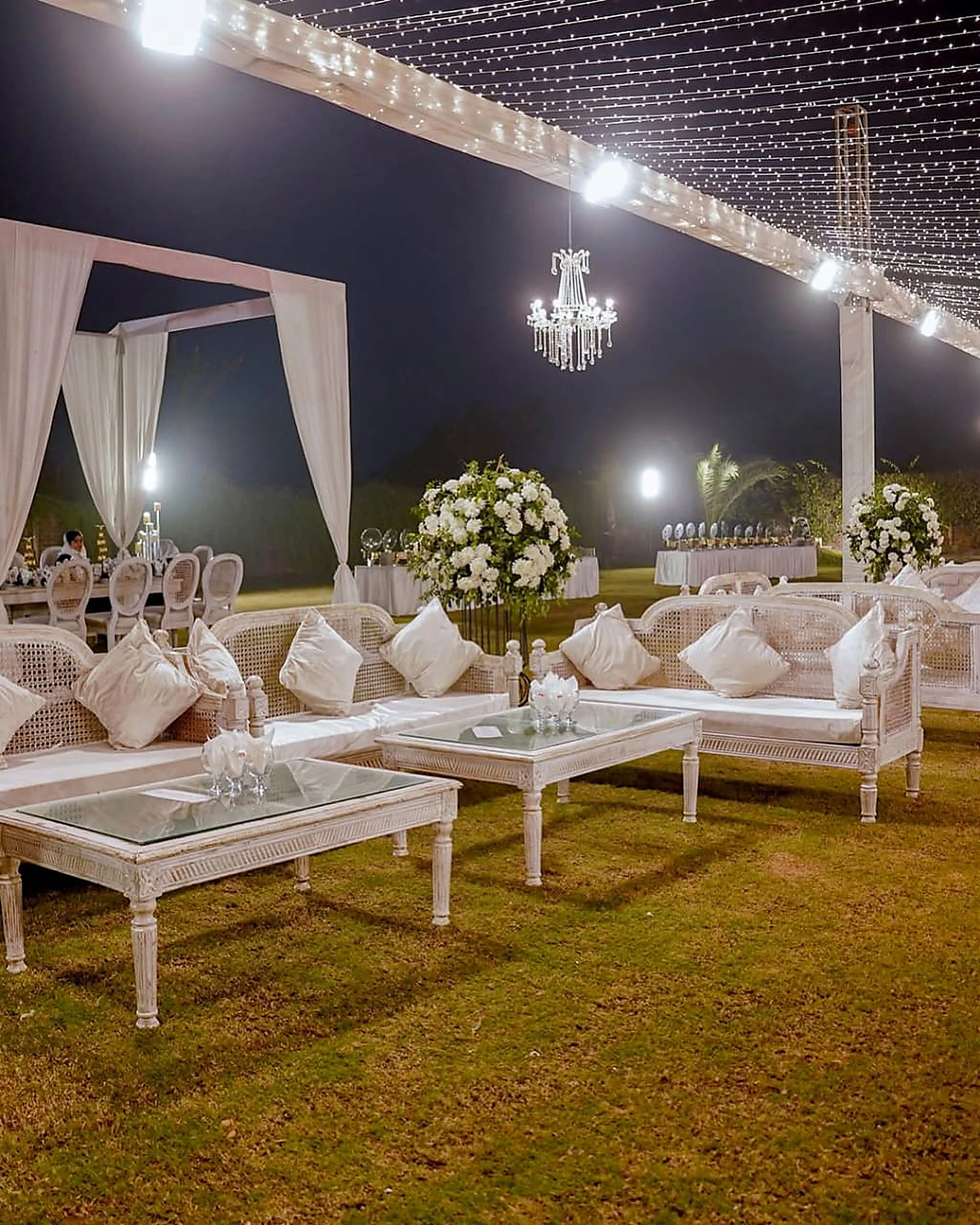 Outdoor evening lounge with white sofas, chandeliers and floral centrepieces