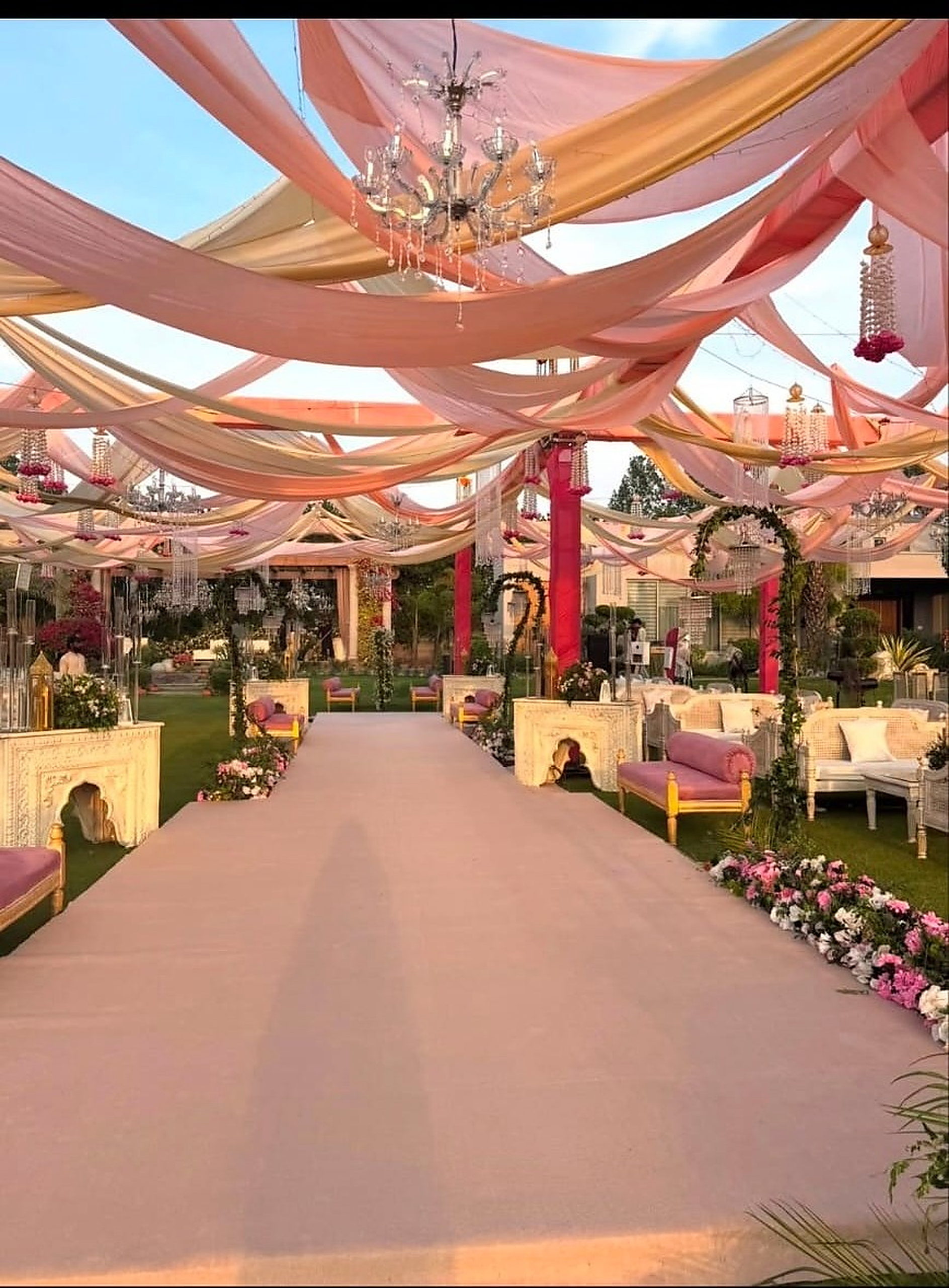 Blush draped canopy over a wide walkway lined with florals and lounge seating