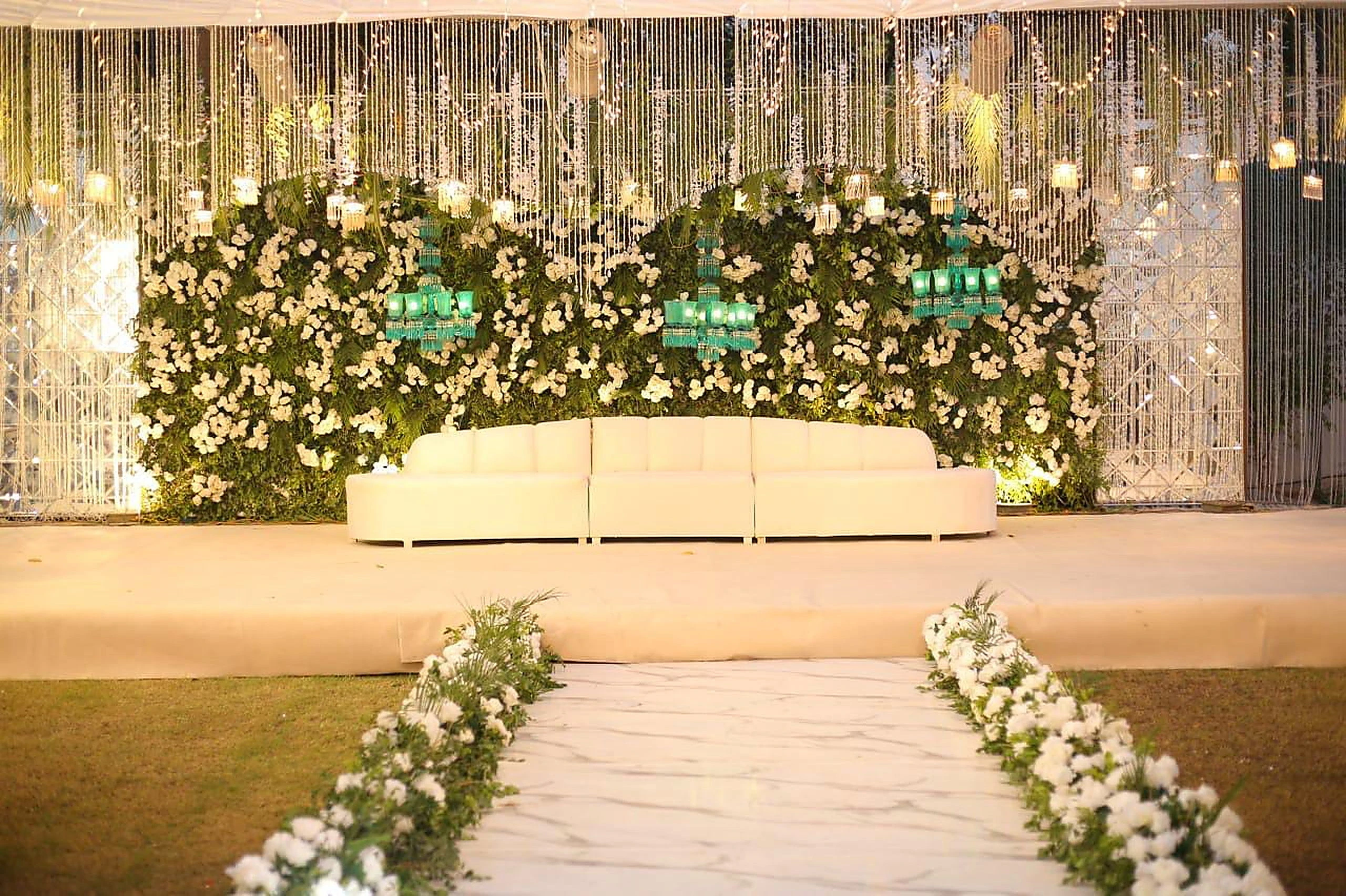 Wide floral stage with white runner aisle and warm evening uplighting