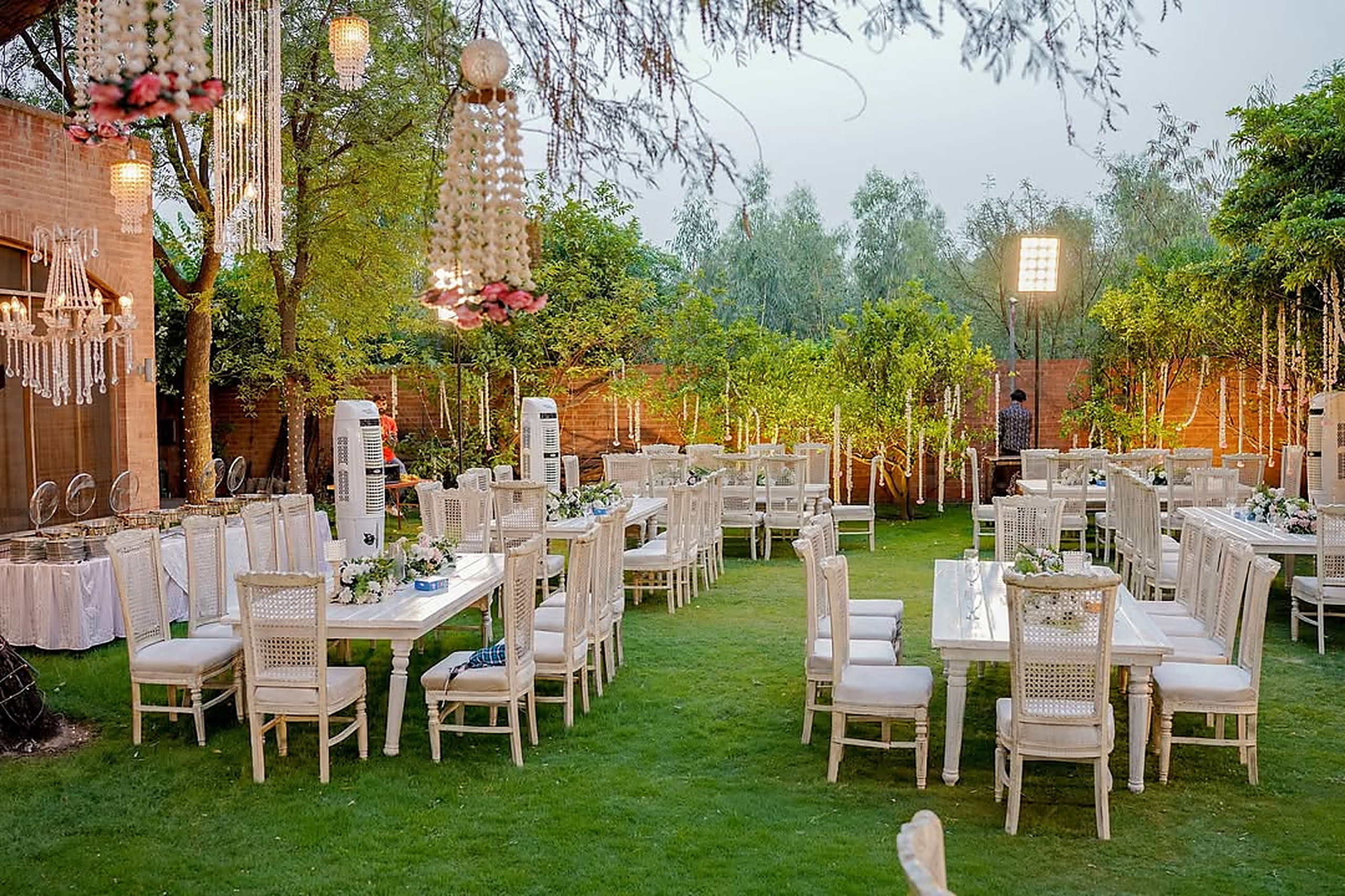 Long banquet tables dressed in white on a garden lawn beneath lantern posts