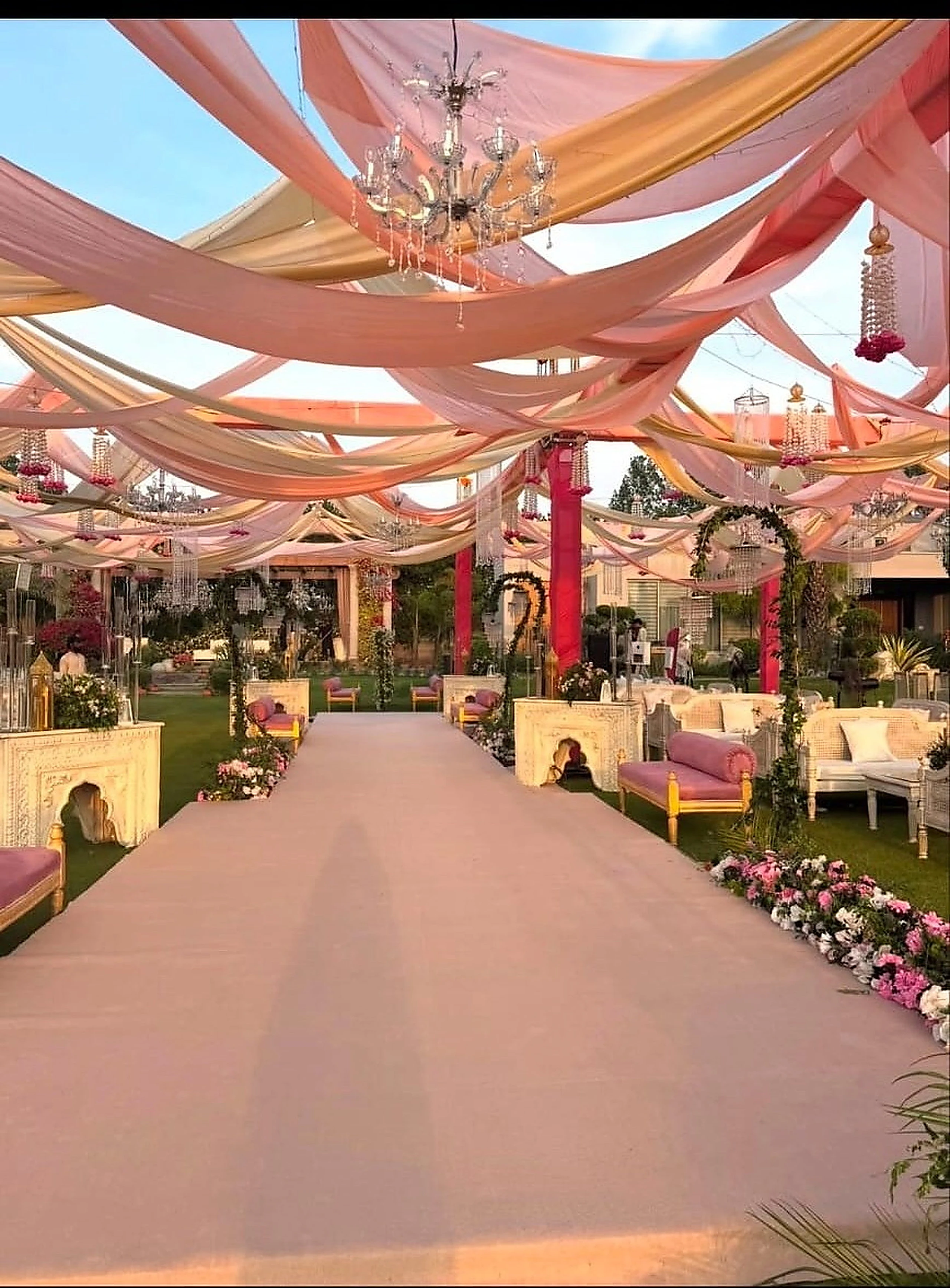 Blush draped canopy over a wide walkway lined with florals and lounge seating