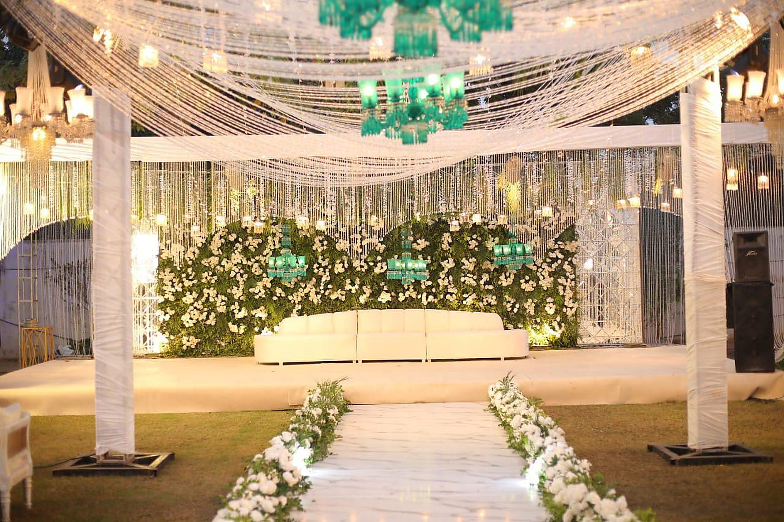 Pillared aisle with crystal drapes and white floral runners leading to a stage