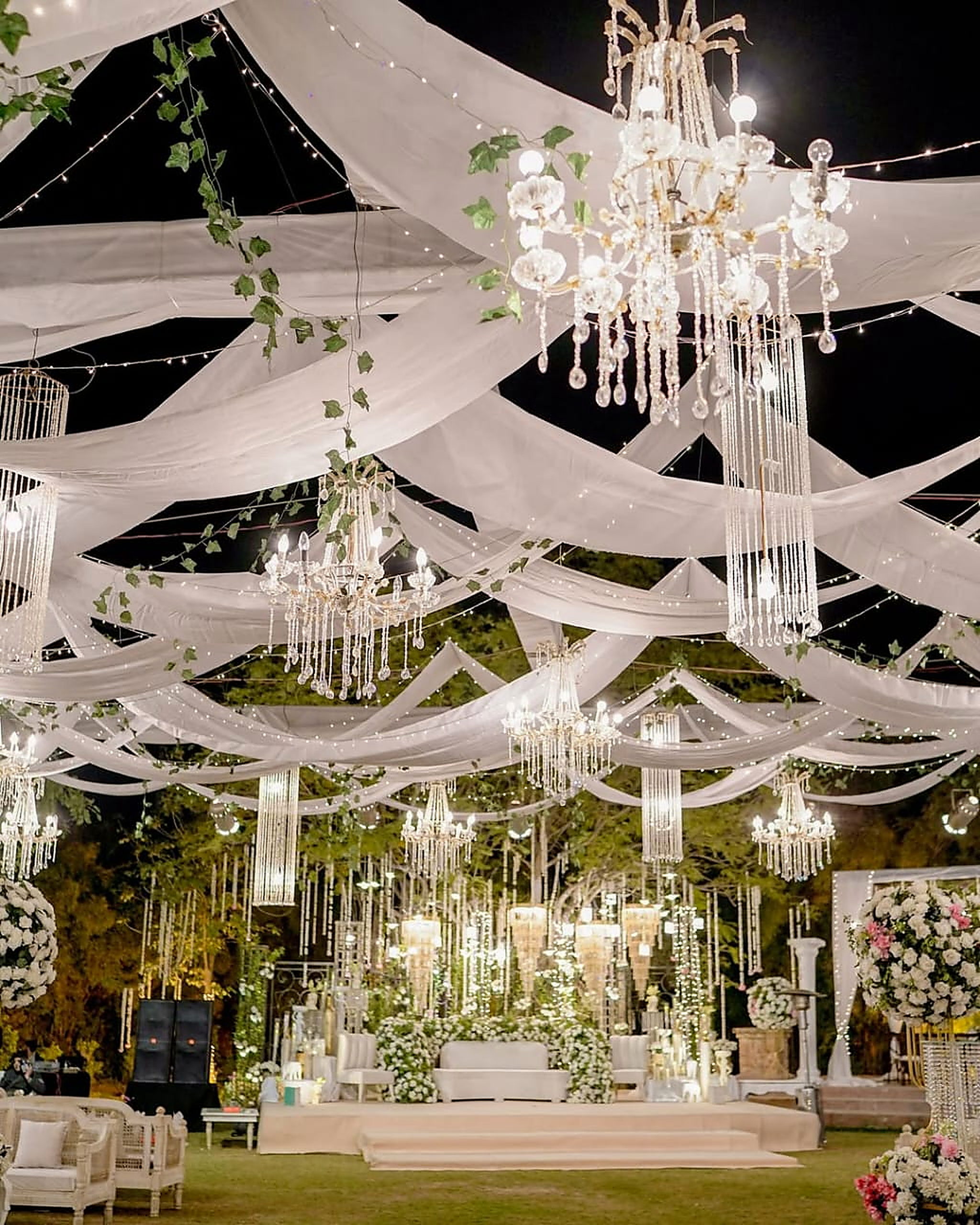 Draped white ceiling and layered chandeliers above a walima stage