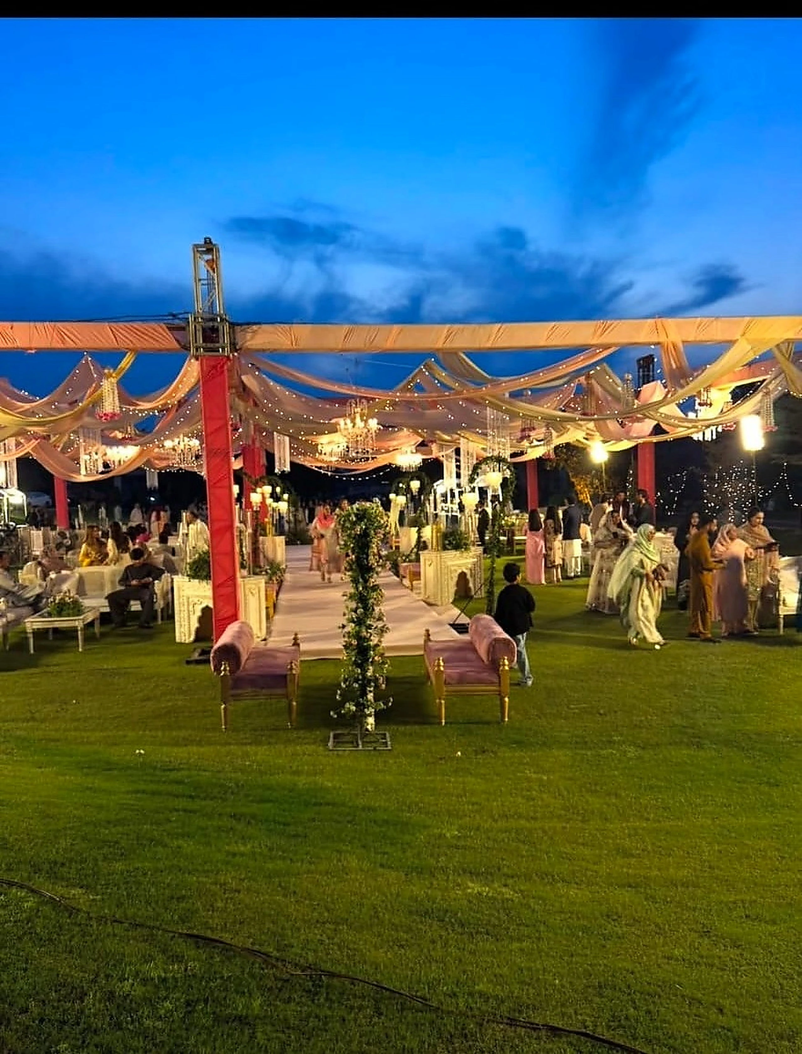 Guests gathered on a lawn beneath a lit canopy at blue hour