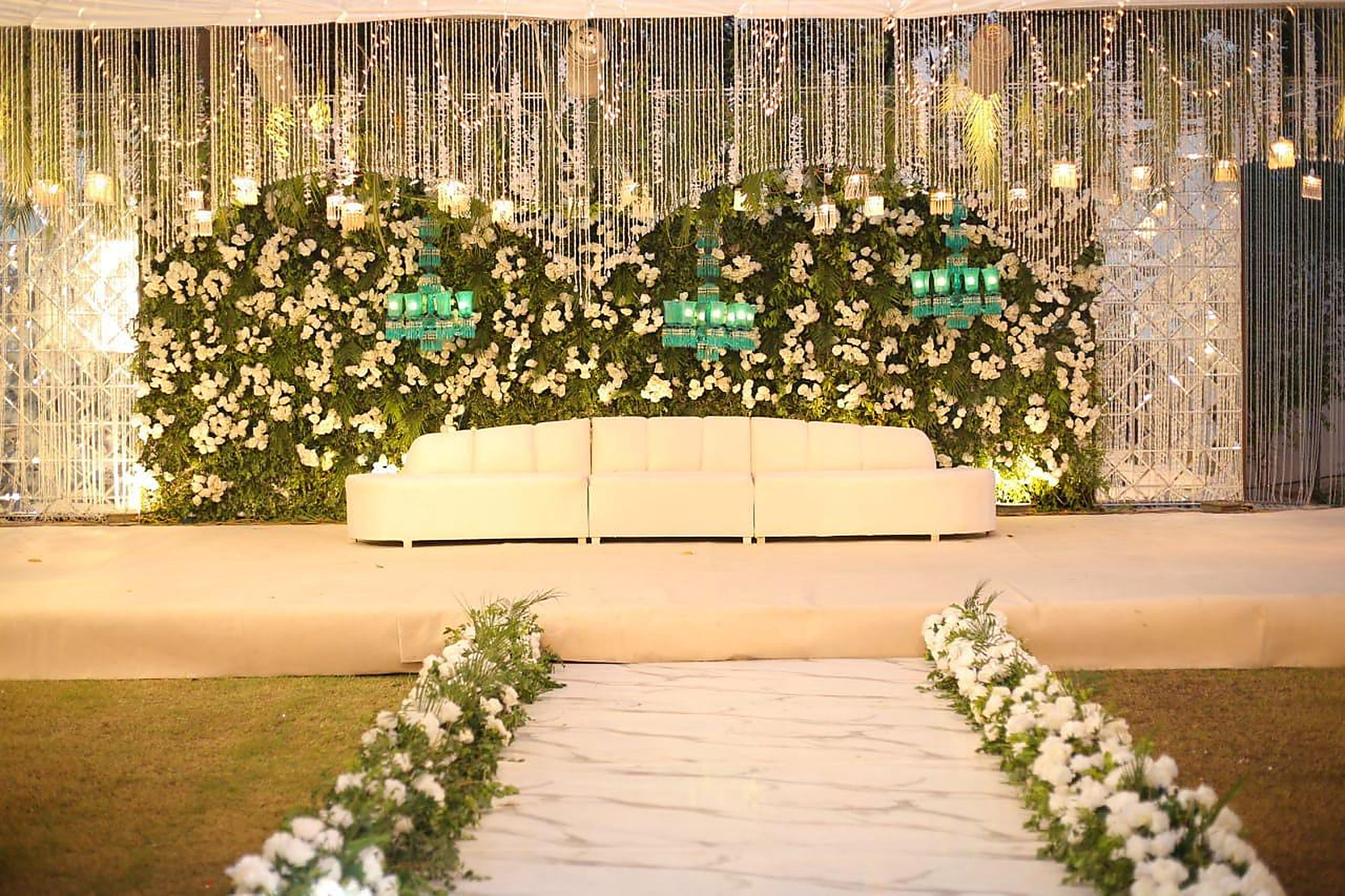 Wide floral stage with white runner aisle and warm evening uplighting