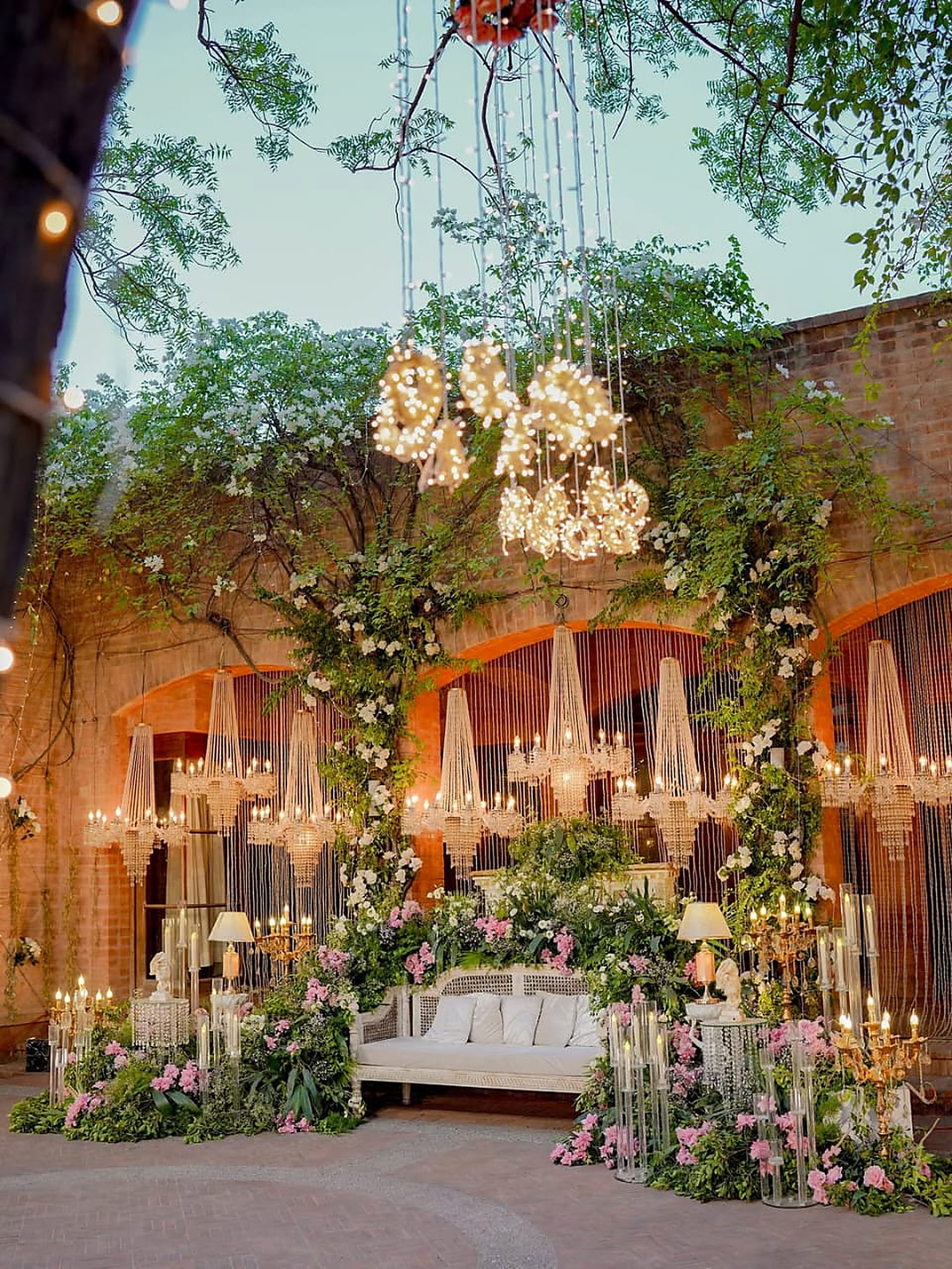Floral wedding stage with hanging blossoms and candlelit console tables at a Lahore farmhouse