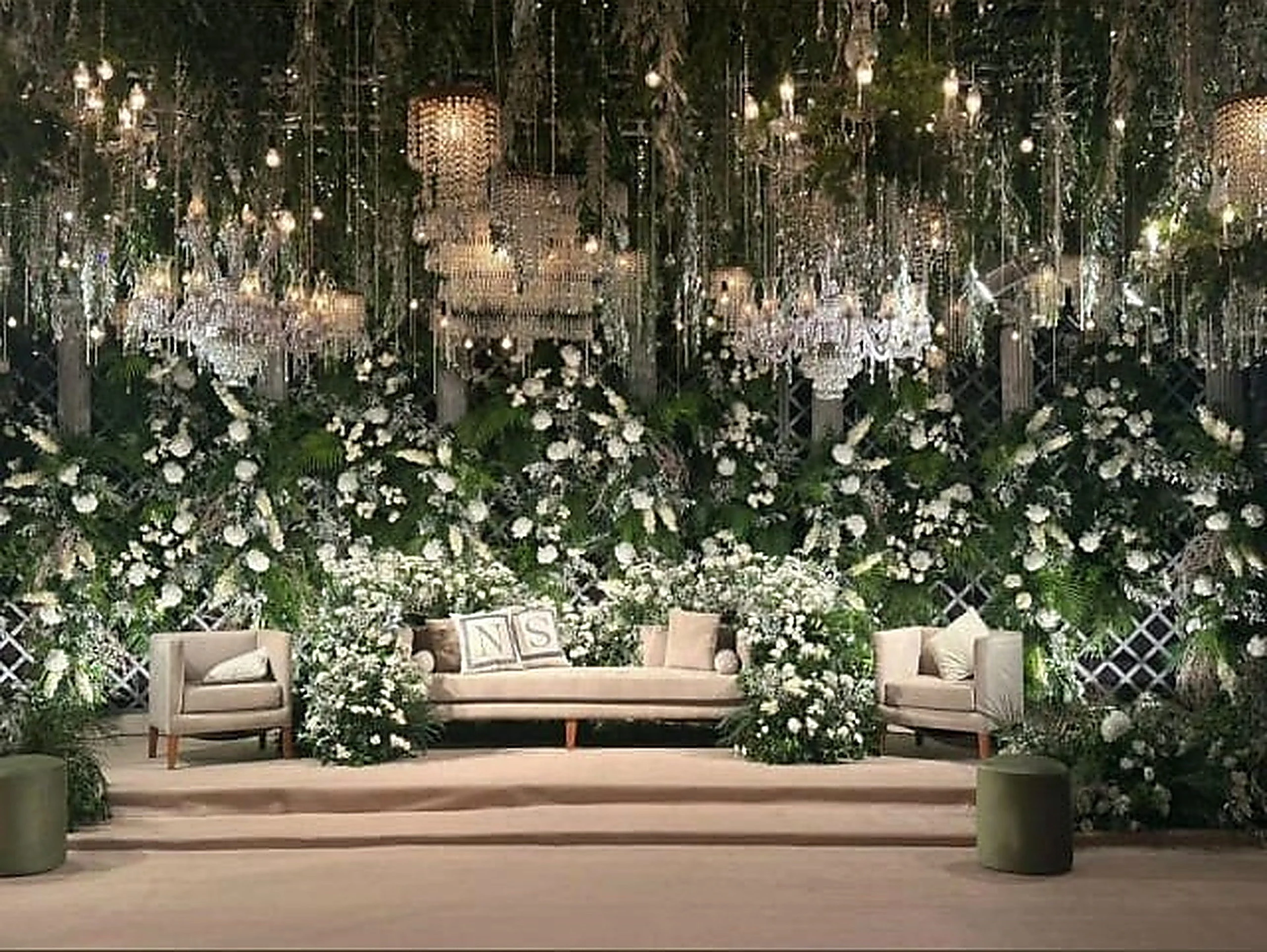 Wide white floral stage with layered hanging greenery and soft uplighting