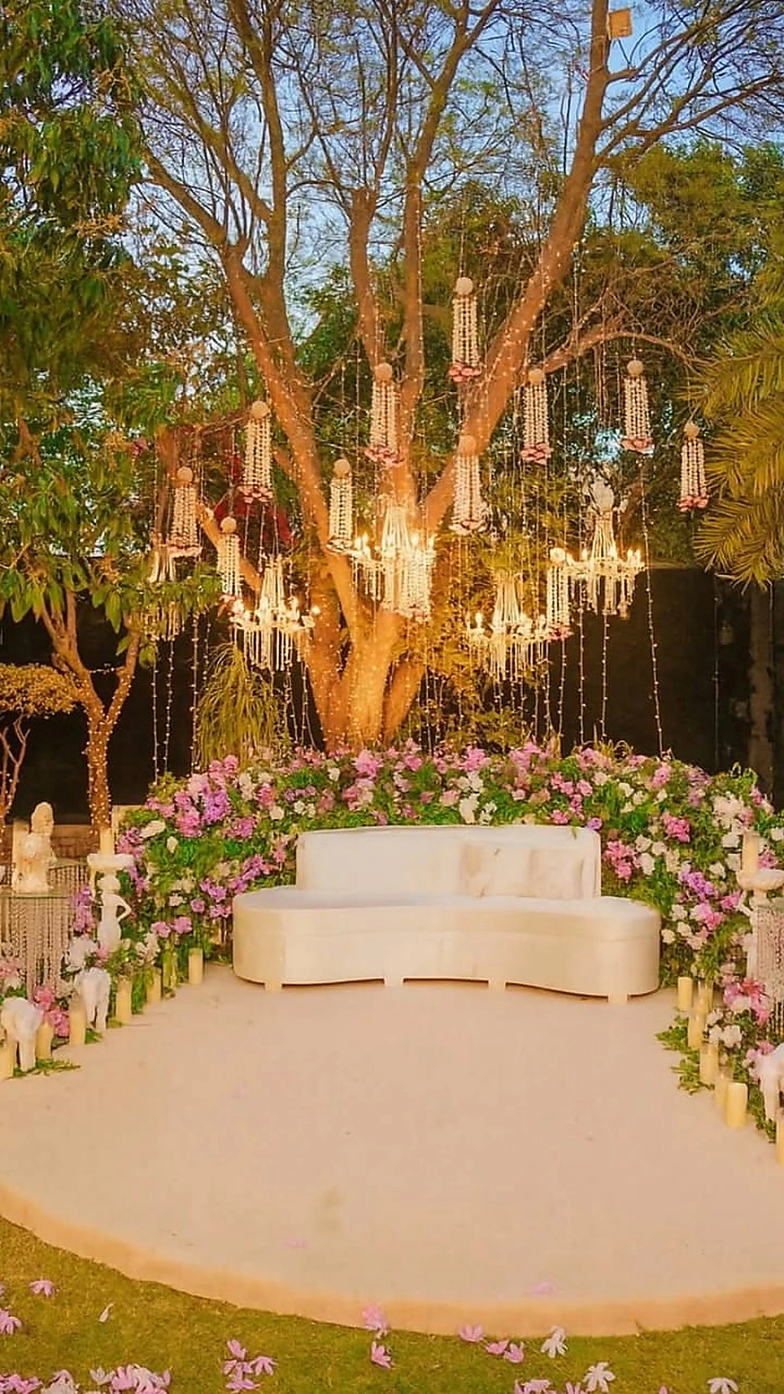 Dusk stage beneath a lit tree with candle columns and pastel florals