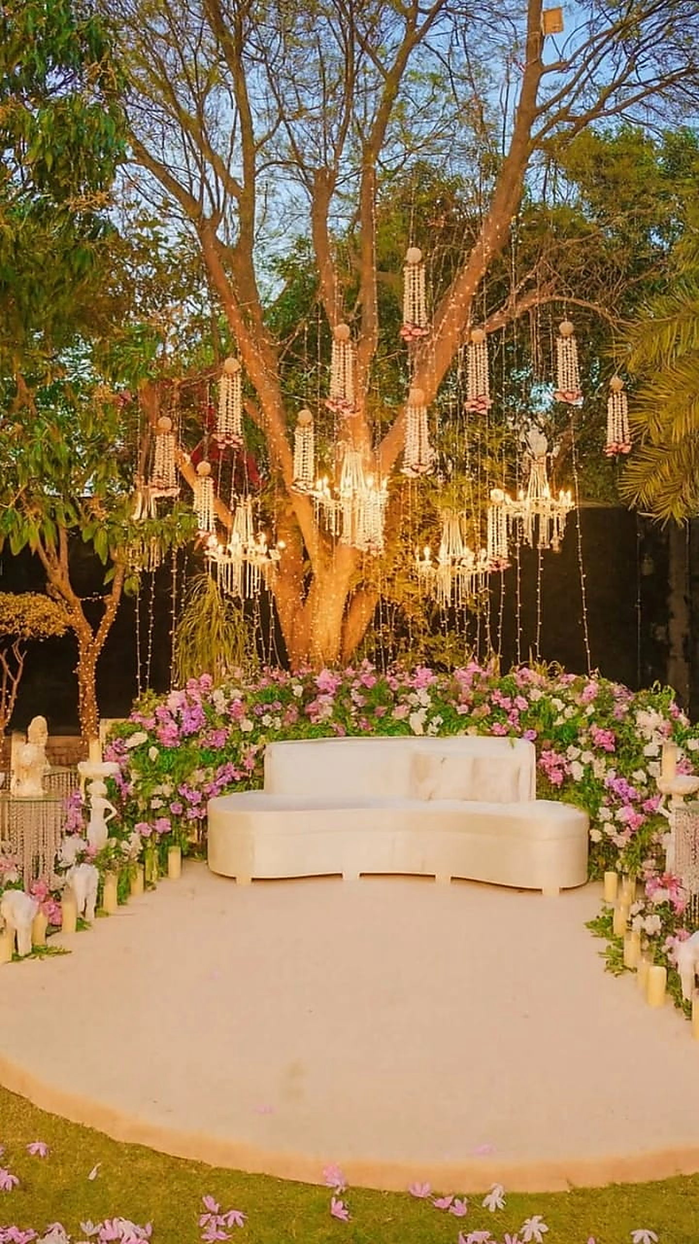 Dusk stage beneath a lit tree with candle columns and pastel florals