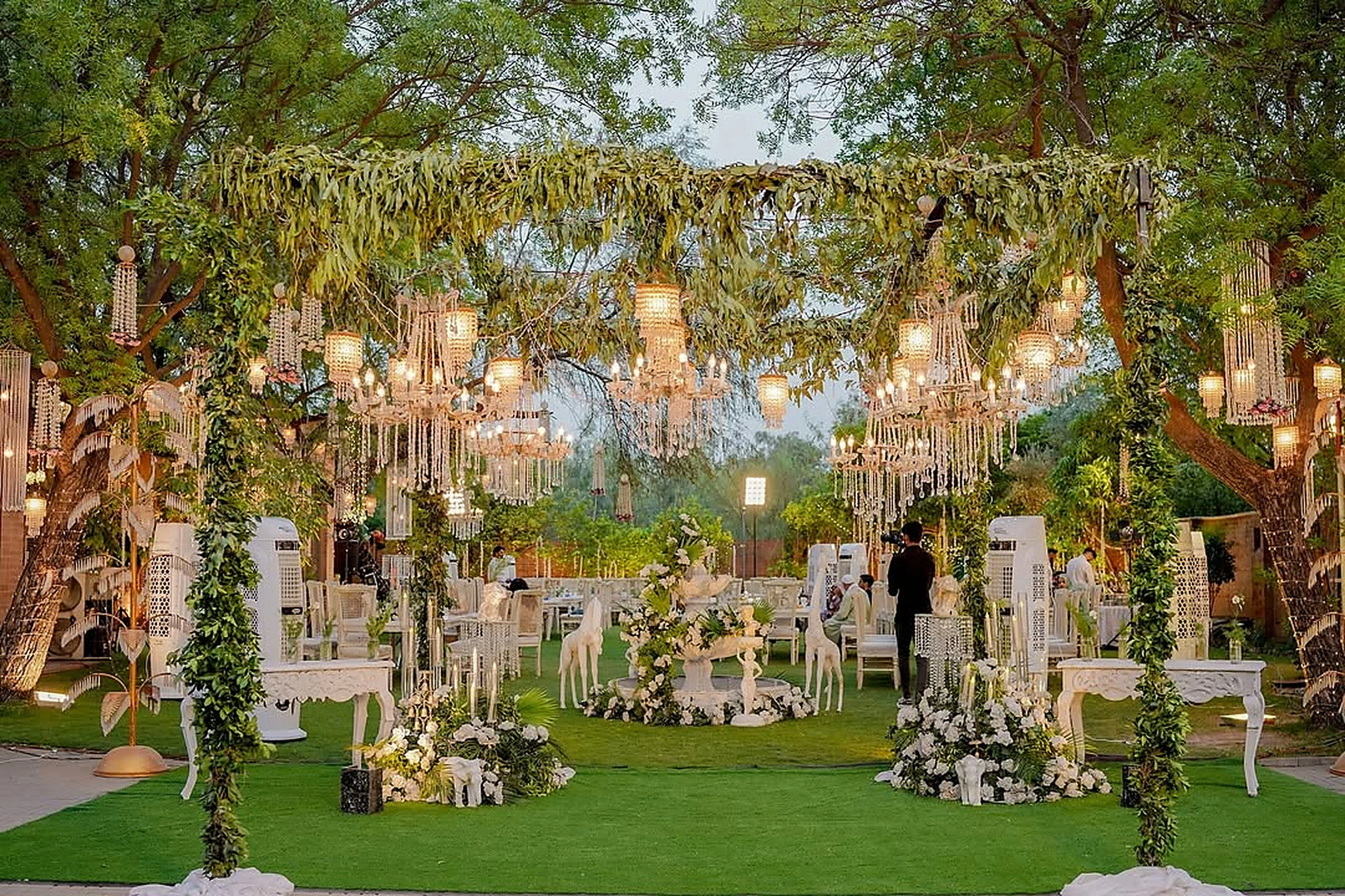 Chandeliers suspended from mature trees above a garden ceremony set